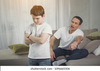 You Are Punished. Irritated Father Is Yelling At His Son. Abused Child Is Standing With Crossed Arms In Room