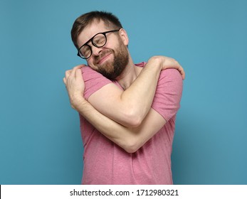 If You Are Single, Hug Yourself. Funny, Cute Bearded Man In Glasses Cuddling Himself And Dreams With Eyes Closed.