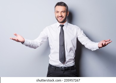 You Are Welcome! Cheerful Mature Man In Shirt And Tie Gesturing Welcome Sign And Smiling While Standing Against Grey Background