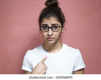 You To Me? Who Am I? Portrait Of A Beautiful Indian Girl In A White T-shirt And Glasses, Questioningly Points At Herself, An Indeterminate Facial Expression.