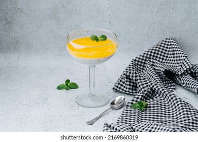 Yougurt Topped With Jelly In A Glass Decorated With Mint Leaf. Next To It Tea Spoon And Piece Of Checkered Cloth On A Table.