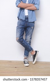Youn man wearing blue jeans with and folding arms ,standing , sneakers on wooden background
