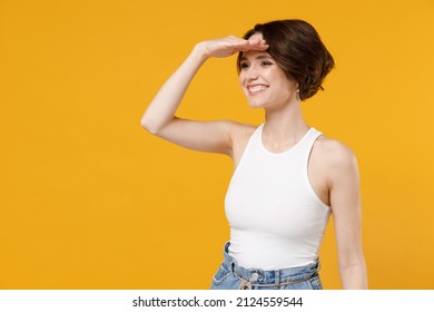 Youn smiling happy caucasian woman 20s with bob haircut wearing white tank top shirt hold hand at forehead look far away distance isolated on yellow background studio portrait People lifestyle concept
