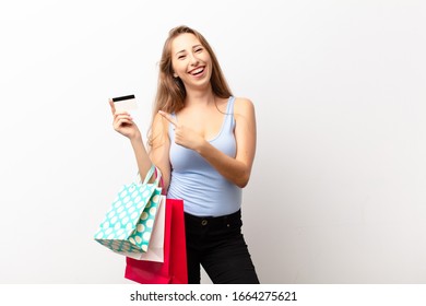 yound blonde woman smiling cheerfully, feeling happy and pointing to the side and upwards, showing object in copy space holding shopping bags - Shutterstock ID 1664275621