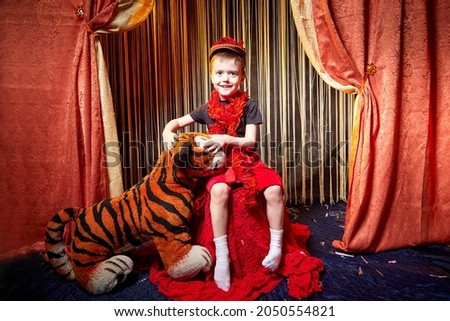 Yound boy during a stylized theatrical circus photo shoot in a beautiful red location. Models small guy posing on stage with circus curtain