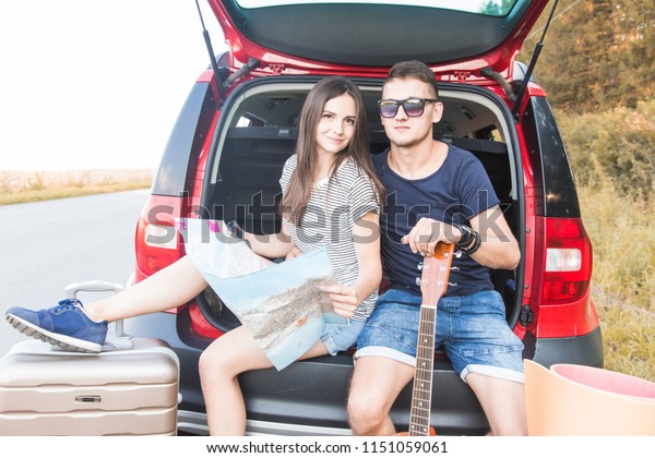 Yound\
Couple with suitcases on a trip by car. They sit in the back of the\
car, they look at the map, resting after a long drive and having\
fun. Hitchhiking and car trips with loved\
one