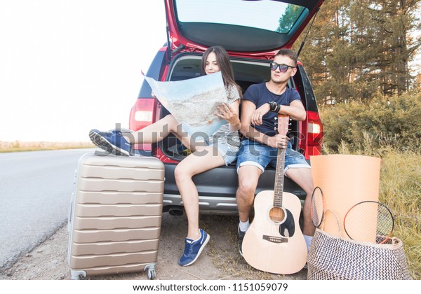 Yound\
Couple with suitcases on a trip by car. They sit in the back of the\
car, they look at the map, resting after a long drive and having\
fun. Hitchhiking and car trips with loved\
one