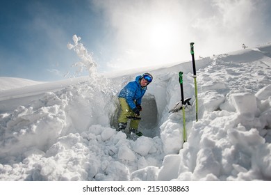 Yound smiling man in bright ski suit with shovel carefully digging the snow. Checking the mountain for avalanche safety.