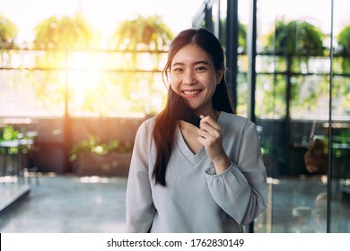 Young 20s Asian Beautiful Woman With Attractive Smile Taking Off Protective Mask (PPE). Professional Business Worker In Modern Office Setting - Corona Virus - Covid 19 New Normal Portrait Concept.