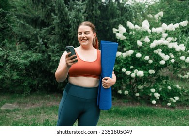 Young 20s fat woman hold yoga mat and using smartphone after workout on street. Portrait of smiling female in sportswear walk using smartphone. High quality photo - Powered by Shutterstock