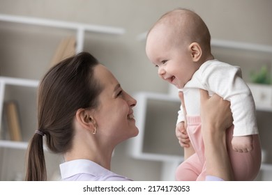 Young 25s Cheerful Loving Mother Lifts Her Adorable Smiling Three-months-old Baby Enjoy Playtime Together At Home, Close Up Shot, Side Profile View. Family Bond, Happy Motherhood, Childcare Concept