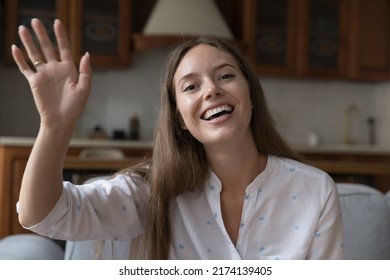 Young 25s Pretty Woman Sit On Sofa At Home Smile Staring At Camera Wave Hand, Start Distance Communication Through Video Call Application, Talk To Family Living Abroad. Virtual Meeting Event Concept