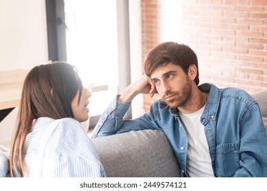 A young 25-year-old couple sits on their cozy sofa in a living room, engaged in a quiet conversation and sharing carefree moments together. Leisure and relaxation concept. Discussion man and woman - Powered by Shutterstock