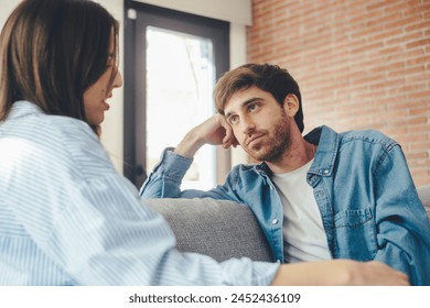 A young 25-year-old couple sits on their cozy sofa in a living room, engaged in a quiet conversation and sharing carefree moments together. Leisure and relaxation concept. Discussion man and woman - Powered by Shutterstock