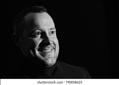 A Young 30 To 45 Year Old Man Looks Smiling, It Looks As If He Is The Man Of An Interview, Black And White Portrait Photo On A Black Background