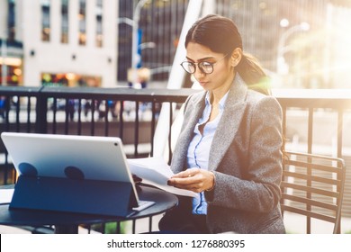 Young 30 Years Old Businesswoman Reading Paper Documents While Sitting Outdoors In City With Touch Pad. Indian Brunette Hair Female Checking Financial Documents And Planning Work Issue During Break