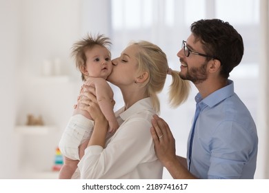 Young 30s loving parents and newborn spend time at home, affectionate mother kisses on cheek baby in diaper, caring father enjoy leisure together with family standing in warm nursery. Love concept - Shutterstock ID 2189741617
