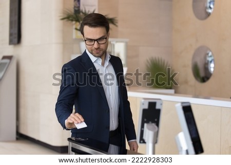 Young 35s businessman in elegant formal suit using pass card to open entrance automatic gates inside modern office building. Door access control keypad with keycard reader in contemporary workplace