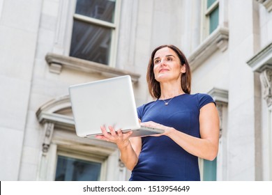 Young 40 Years Old Native American Businesswoman Working In New York City, Wearing Short Sleeve Dress, Holding Laptop Computer, Standing Outside Office Building With Windows, Looking Up, Thinking.