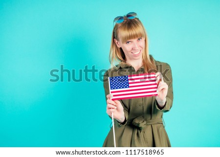 young and active blonde woman holds American flag in studio on blue background