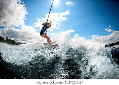 Young Active Cheerful Woman Riding On The Wake Surf Holding Rope Of Motorboat And Water Splashing Around.