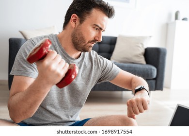 Young active man checking time in smartwatch during home trainings