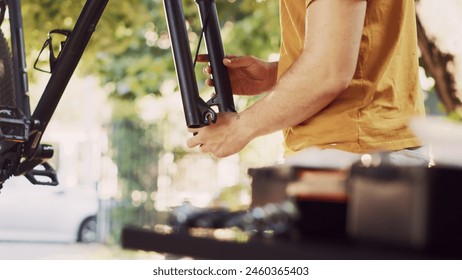 Young active man delicately detaching wheel and fine-tuning bike front fork and headset for safe outdoor cycling. Close-up of male cyclist repairing and adjusting broken modern bicycle. - Powered by Shutterstock