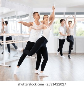 Young active man engaged in dance hall with female partner and practicing ballet arabesque pose during group class. Hobby, healthy lifestyle concept - Powered by Shutterstock