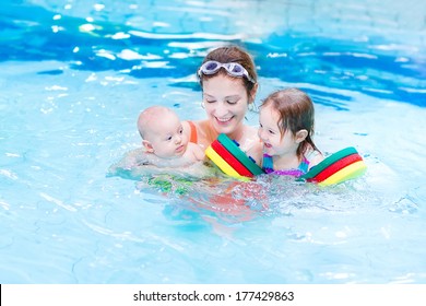 Young Active Mother Having Fun In A Swimming Pool With Two Kids, A Newborn Baby Boy And A Cute Happy Toddler Girl