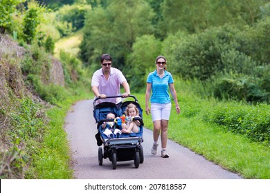 Young active parents hiking in the mountains with a double twin stroller with two children, brother and sister, baby boy and toddler girl