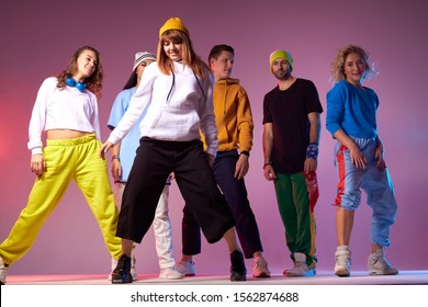 Young Active People Dressed In Casual Sport Outfit, Standing In Full Length On Dance Studio Floor, Expressing Confidence Over Pink Background, Shot From Below