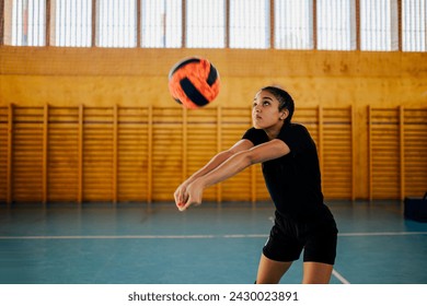 A young active sportswoman is hitting and passing a ball on court during her volleyball training. Portrait of a multicultural female teenage volleyball player hitting a ball on training on court. - Powered by Shutterstock