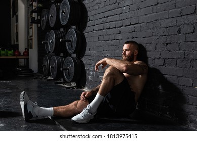 Young active strong sweaty fit muscular man with big muscles sitting on the gym floor and taking a break from hardcore cross workout training real people
