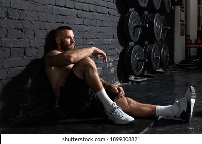 Young active strong sweaty fit muscular man with big muscles sitting on the gym floor and taking a break from hardcore cross workout training real people