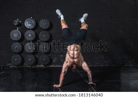 Young active strong sweaty fit muscular man with big muscles doing hand stand and walk in the gym as hardcore crossfit workout training real people exercising