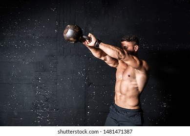 Young active strong sweaty focused fit muscular man with big muscles holding heavy kettlebell for swing cross training hard core workout in the gym real people exercising