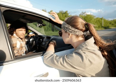 Young active woman with long blond hair talking to driver through vehicle window while standing on highway during trip - Powered by Shutterstock