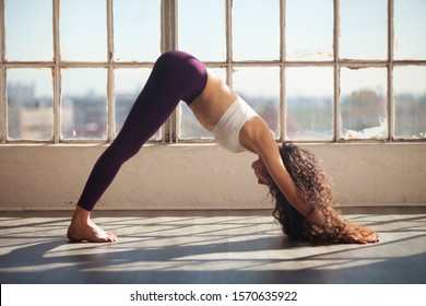 Young active woman practicing yoga by large open window in downward facing dog position. Caucasian woman in her 20s performing Adho Mukha Svanasana - Powered by Shutterstock