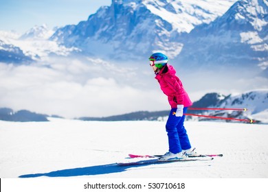 Young Active Woman Skiing In Mountains. Female Skier Kid With Safety Helmet, Goggles And Poles Enjoying Sunny Winter Day In Swiss Alps. Ski Race For Adults. Winter And Snow Sport In Alpine Resort