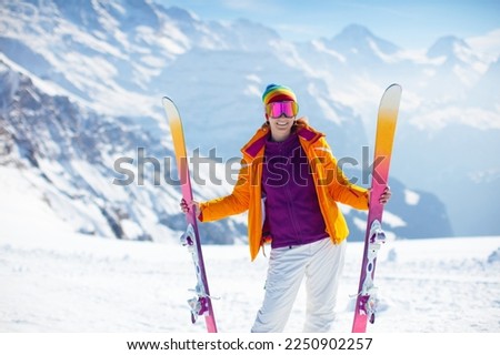 Young active woman skiing in mountains. Female skier with safety helmet, goggles and poles enjoying sunny winter day in Swiss Alps. Ski race for adults. Winter and snow sport in alpine resort.