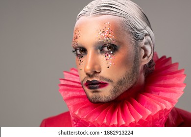 Young Actor With Stage Makeup, White Hair In Accurate Hairdo And Red Paper Jester Collar Around Neck Looking At You Against Grey Background