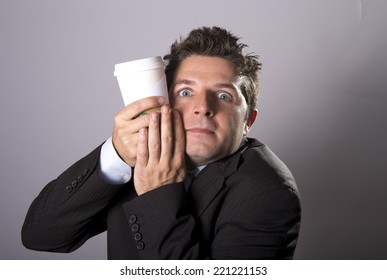 young addict business man in suit and tie holding cup of take away coffee against crazy maniac face in caffeine addiction isolated on grey background