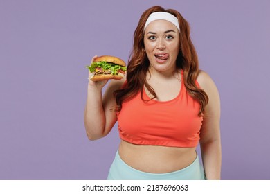 Young Addicted Caucasian Chubby Overweight Plus Size Big Fat Fit Woman In Red Top Warm Up Training Hold Fast Food Burger Lick Lips Isolated On Purple Background Gym Workout Sport Motivation Concept