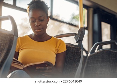 Young adorable african american joyful woman sitting in a bus and reading a book. Public transportation and people concept. Copy space. Diverse portrait.