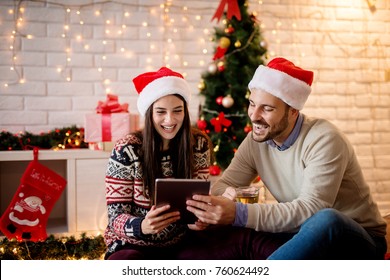 Young adorable smiling couple buying online while sitting on the floor and drinking tea for Christmas.