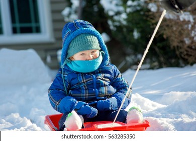 young adorable toddler boy riding on sled in the snow during winter