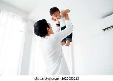 Young adult 30s Asian father lifting his little own son up flying in the air in bedroom at home. Family time and fatherhood concept in Asia