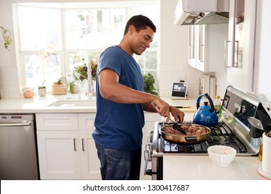 Young adult African American man standing in the kitchen cooking on the hob, using a spatula and frying pan, side view, close up - Powered by Shutterstock