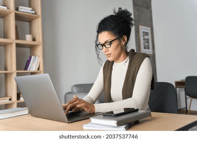 Young adult African American mixed race student wearing glasses sitting at desk with notebooks and laptop computer working typing at home modern living room. Remote distant e learning work concept.