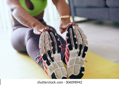 Young adult african american woman in sports clothing at home, doing domestic fitness and training on yellow pad. The girl does muscular legs stretching touching feet with hands